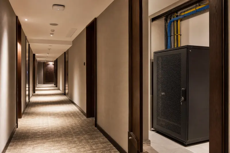 Guest-floor corridor with wireless endpoint and recessed telecom cabinet.
