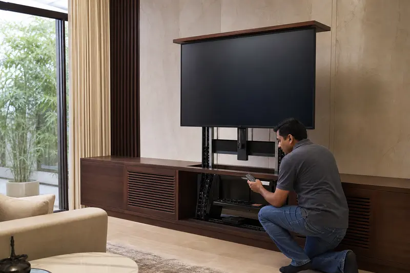 Technician commissions a cabinet television lift with its support rails exposed.