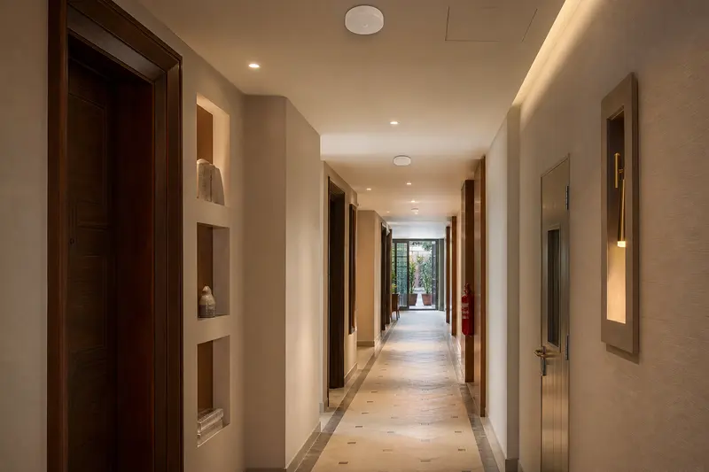 Long hotel corridor with multiple restrained ceiling access points and varied wall geometry.