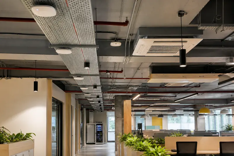Open-plan office showing distributed ceiling access points, cable containment and a distant network cabinet.