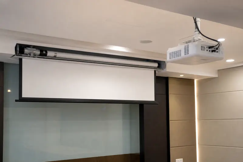 A motorized projection screen operates with its tubular motor visible for service.